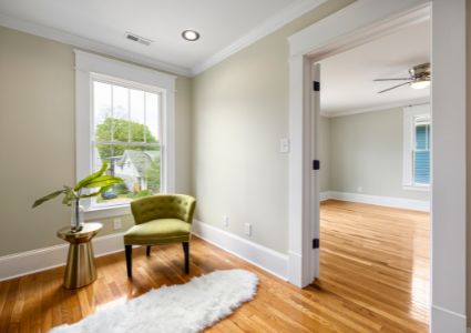 The cream and wooden interior of a house is pictured with a green chair and plant.